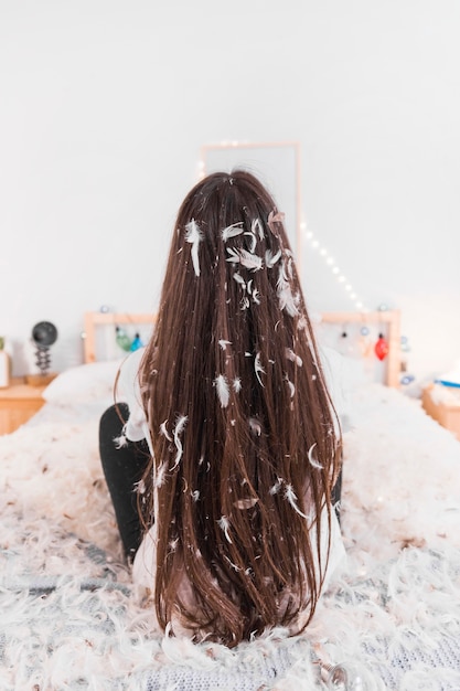 Bezpłatne zdjęcie tylni widok kobiety obsiadanie na łóżku z białym piórkiem w brunetce długie włosy