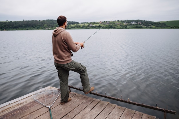 Tylni widok mężczyzna pozycja na mola połowie w jeziorze