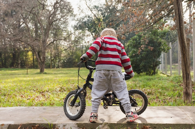 Tylni widok mężczyzna pozycja z bicyklem w parku