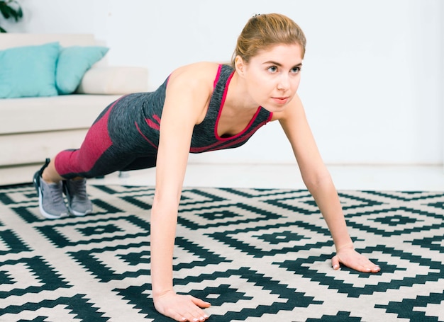 Bezpłatne zdjęcie ufna młoda kobieta robi pushups na dywanie w żywym pokoju