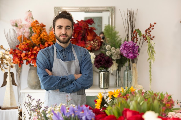 Ufna uśmiechnięta młoda męska kwiaciarnia z kolorowymi kwiatami w jego sklepie