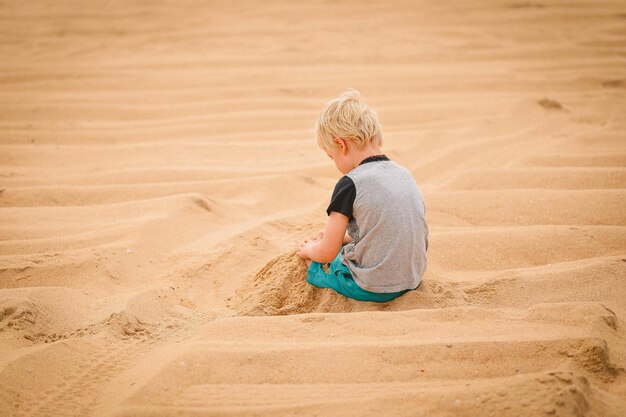 Ujęcie dziecka o jasnych włosach bawiącego się w piasku, tyłem do aparatu