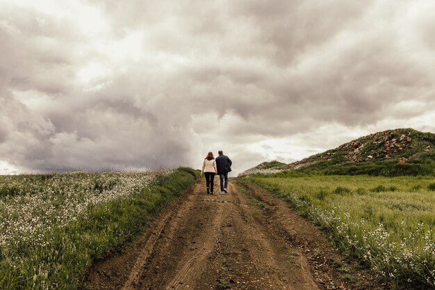 Ujęcie mężczyzny i kobiety idących ścieżką w dolinie z kwiatami pod mglistym niebem