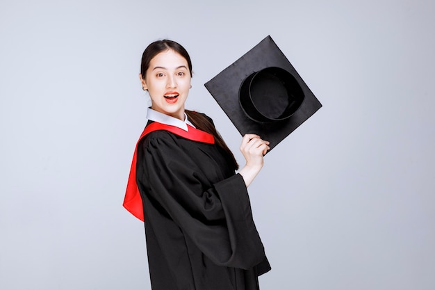 Ujęcie młodej studentki w sukni pokazującej jej czapkę dyplomową. zdjęcie wysokiej jakości