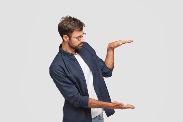 Ujęcie z ukosa pewnego siebie mężczyzny ukazuje rozmiar lub wysokość czegoś, unosi dłonie w powietrze