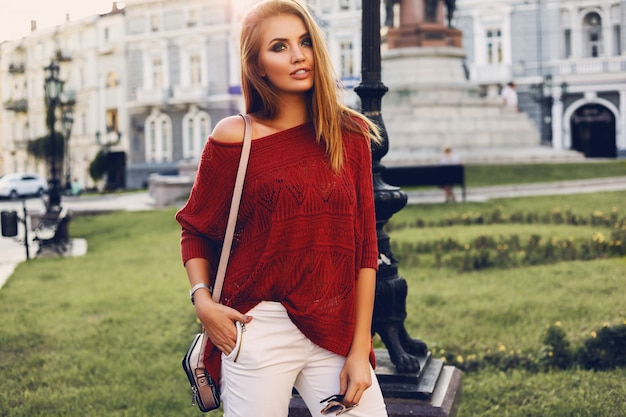 Uliczny portret młodej pięknej eleganckiej kobiety w czerwonym swetrze.