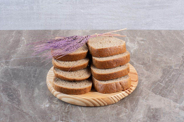 Ułożone kromki ciemnego chleba i fioletowa łodyga pszenicy na tacy na marmurowym tle. Zdjęcie wysokiej jakości