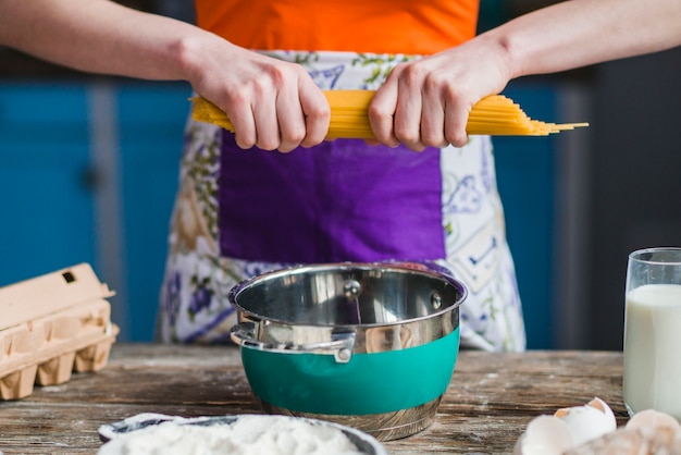 Bezpłatne zdjęcie uprawa kobieta pękanie spaghetti na rondlu