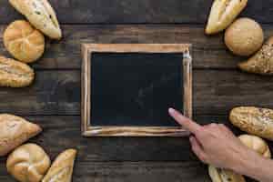 Bezpłatne zdjęcie uprawy ręka wskazuje przy blackboard blisko chleba