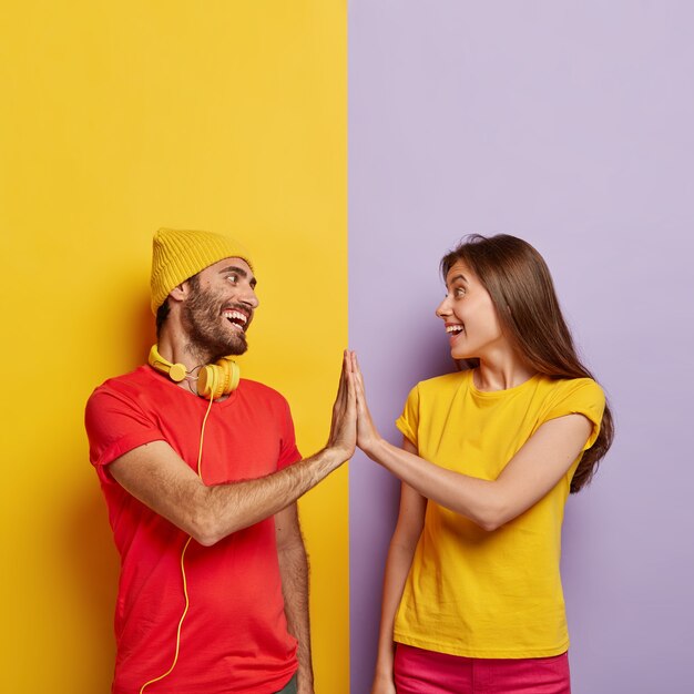 Uradowany chłopak i dziewczyna dotykają dłońmi, uśmiechają się pozytywnie, zgadzają się w czymś, ubrani w czerwono-żółte casualowe koszulki