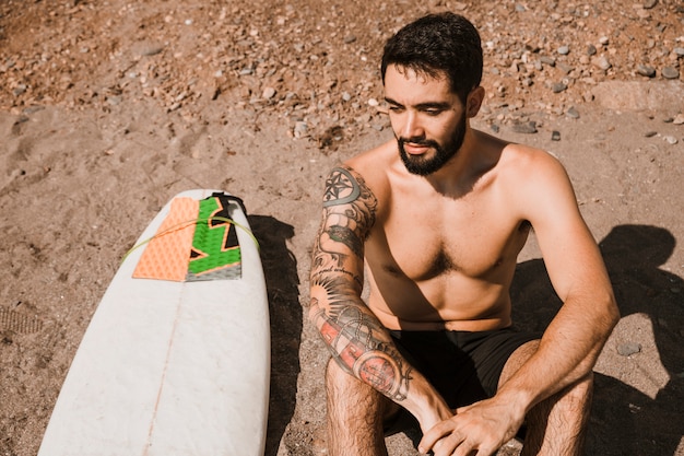 Uradowany mężczyzna siedzi w pobliżu deski surfingowej