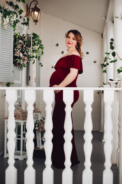Bezpłatne zdjęcie urocza kobieta w ciąży w sukience marsala pozuje na schodach domu