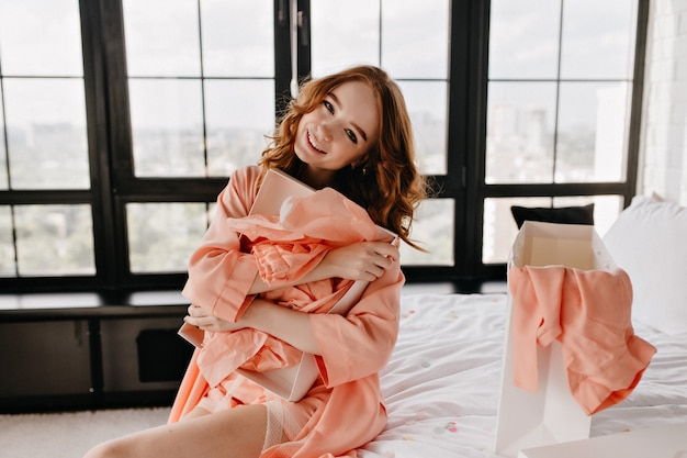 Urocza kręcona dziewczyna śmiejąca się w swojej sypialni. Niesamowita ruda dama w piżamie siedząca na łóżku.