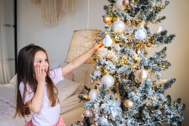 Urocza mała dziewczynka dekoruje choinkę bombkami w domu