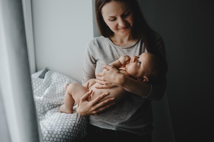 Bezpłatny plik Zdjęcie urocza mama trzyma szczęśliwą nowonarodzoną chłopiec pozycję przed jaskrawym okno
