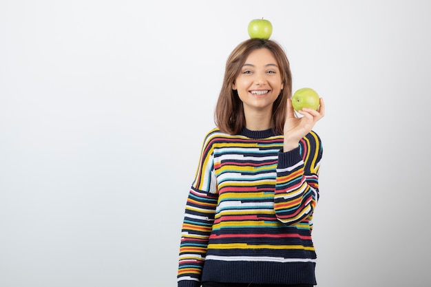 Urocza młoda dziewczyna w ubranie trzyma zielone jabłka na białym tle.