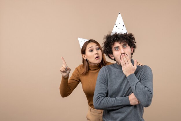 Urocza młoda para nosi kapelusz nowy rok zły dziewczyna patrząc stojąc za zszokowanym facetem na szaro