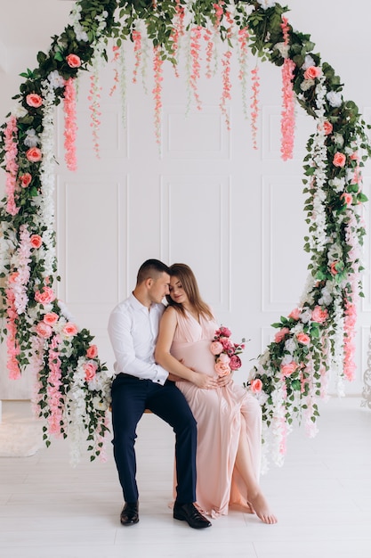 Urocza młoda para spodziewa się w białym studiu bogatym ozdobionym różowymi kwiatami