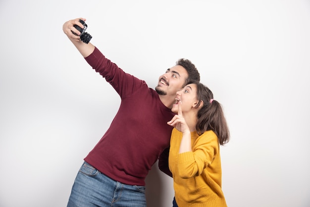 Urocza Para Robi Selfie Z Aparatem I Pozuje Nad Białą ścianą.