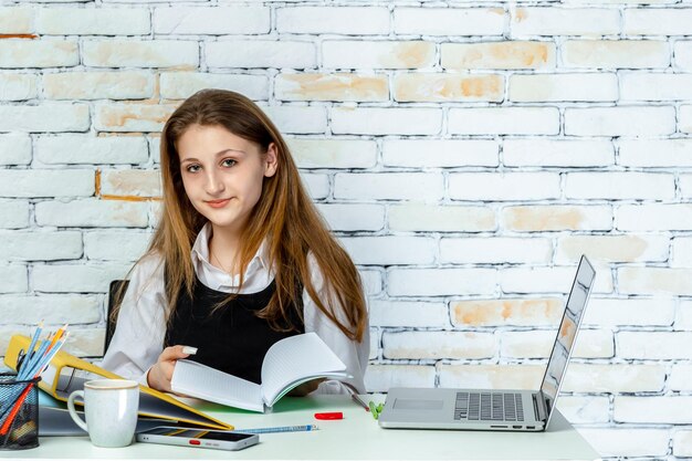 Urocza studentka siedząca za biurkiem i patrząca w kamerę Zdjęcia wysokiej jakości