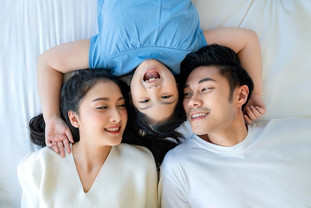 Uroczi azjatyccy rodzice rodziny i córka bawiące się w sen na białym miękkim łóżku wraz ze szczęściem i wesołą wakacyjną poranną aktywnością koncepcją domu rodzinnego