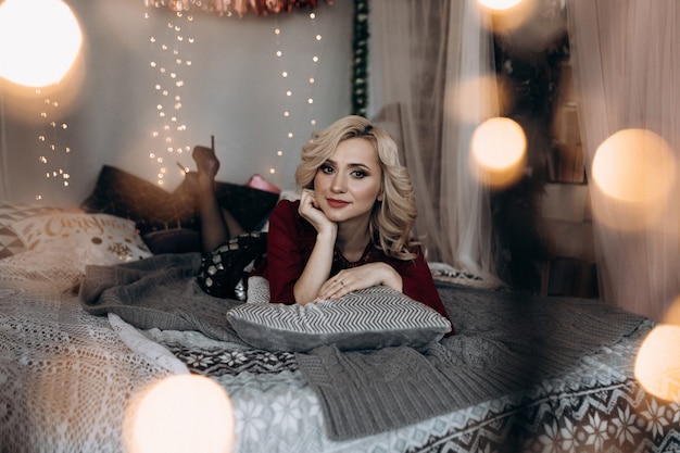 Bezpłatne zdjęcie uroczy blondynka kobieta koperty się w szare kratę siedzi na łóżku przed choinką
