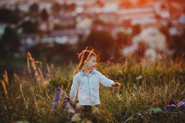 Uroczy mały chłopiec chodzi z poduszką po zielonym trawniku