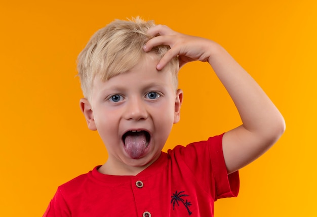 Uroczy mały chłopiec o blond włosach i niebieskich oczach na sobie czerwoną koszulkę, trzymając rękę na głowie z otwartymi ustami