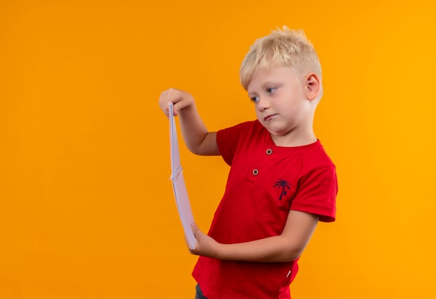 Bezpłatne zdjęcie uroczy mały chłopiec o blond włosach i niebieskich oczach ubrany w czerwoną koszulkę patrząc na notebooka