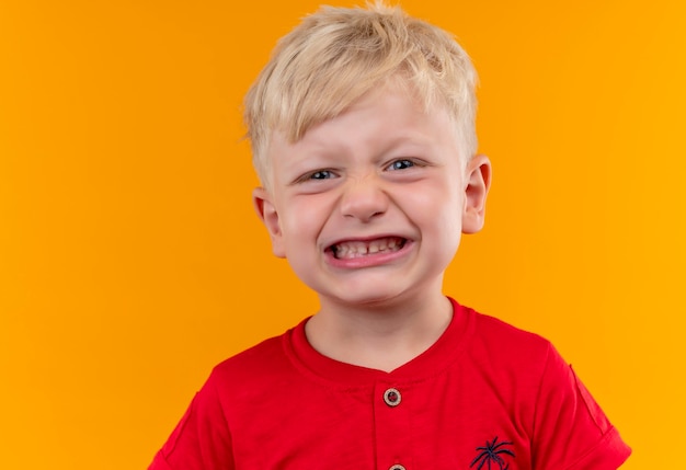 Uroczy mały chłopiec o blond włosach i niebieskich oczach ubrany w czerwoną koszulkę z zębami