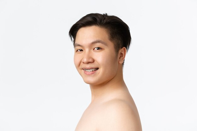 Uroda Pielęgnacja skóry i higiena koncepcja zbliżenie uśmiechniętego nagiego azjatyckiego mężczyzny z szelkami stojącego nago...