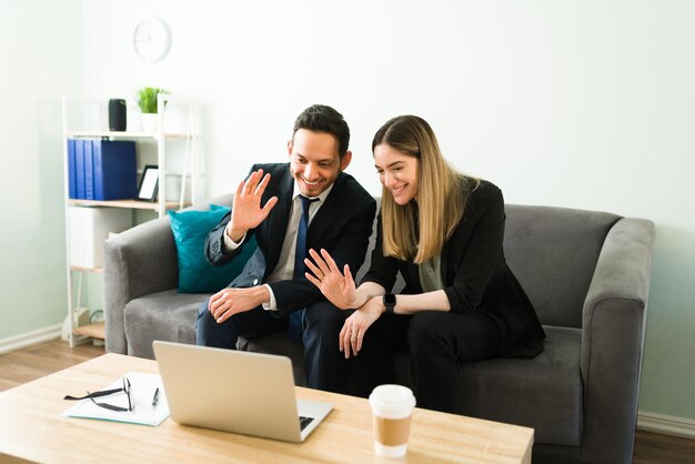 Uśmiechnięci partnerzy biznesowi machający i witający się ze współpracownikami i współpracownikami podczas rozmowy wideo na laptopie. Biznesowa kobieta i mężczyzna podczas spotkania online w biurze