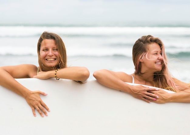 Uśmiechnięci przyjaciele na plaży z deską surfingową