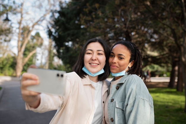 Bezpłatne zdjęcie uśmiechnięci przyjaciele ze średnim strzałem robiący selfie na zewnątrz