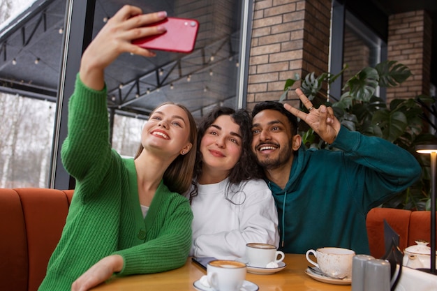 Bezpłatne zdjęcie uśmiechnięci przyjaciele ze średnim strzałem ze smartfonem