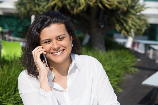 Uśmiechnięta atrakcyjna kobieta opowiada na telefonie komórkowym outdoors