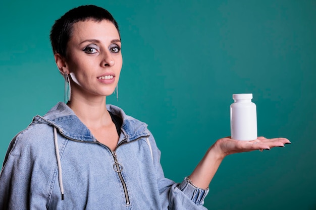 Bezpłatne zdjęcie uśmiechnięta atrakcyjna kobieta trzymająca butelkę pigułek prezentująca produkt opieki zdrowotnej przed kamerą, stojąc nad odizolowanym tłem w studio. wesoła kobieta recenzująca suplement farmaceutyczny