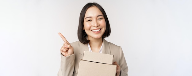 Uśmiechnięta azjatycka sprzedawczyni wskazująca palcem na miejsce na kopię, trzymająca pudełka z zamówieniem dostawy stojącym na białym tle
