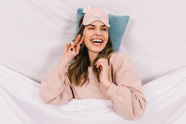 Bezpłatne zdjęcie uśmiechnięta błoga kobieta w piżamie, leżąc w łóżku