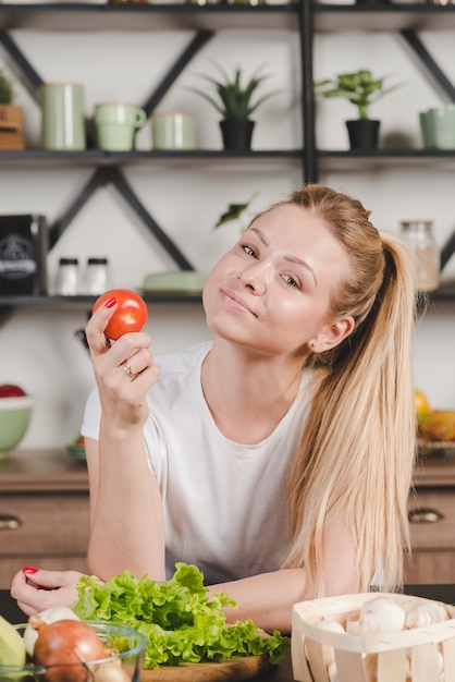 Uśmiechnięta blondynki młoda kobieta trzyma czerwonego pomidoru w ręce