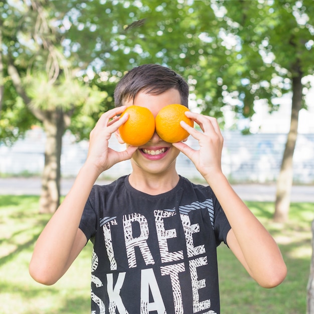 Uśmiechnięta chłopiec zakrywa ona oczy z świeżymi całymi pomarańczami w parku