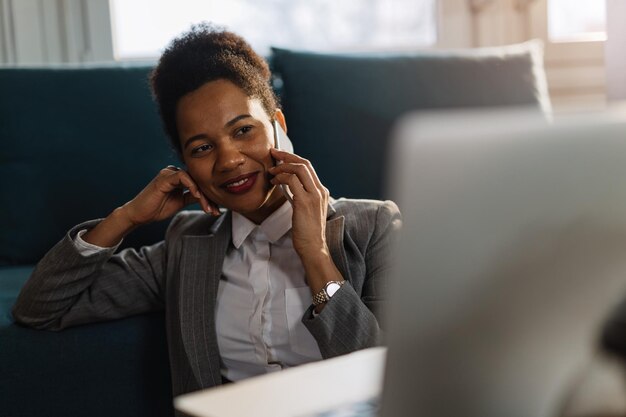 Uśmiechnięta czarna bizneswoman pracuje w domu i rozmawia z kimś przez telefon komórkowy