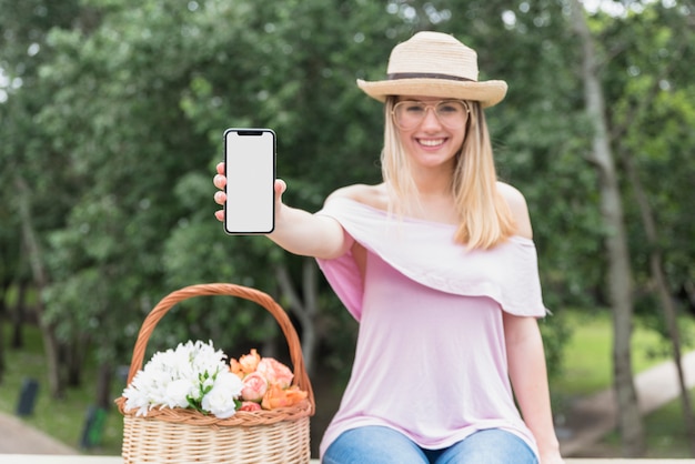 Uśmiechnięta dama w eyeglasses i kapeluszu pokazuje telefon komórkowego