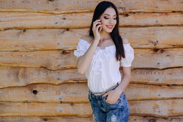 Uśmiechnięta dziewczyna przechylony na drewnianej ścianie rozmawia przez telefon