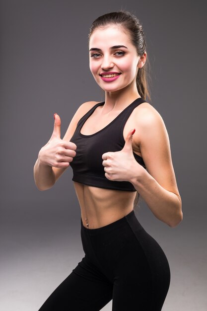 Uśmiechnięta kobieta fitness pokazując kciuk znak na szarej ścianie