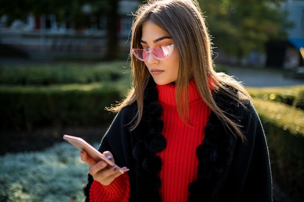 Uśmiechnięta kobieta idzie ulicą w Central Parku i używa telefonu