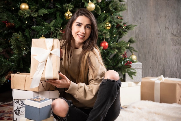 Uśmiechnięta kobieta leżąc na puszystym dywanie z prezentami świątecznymi.