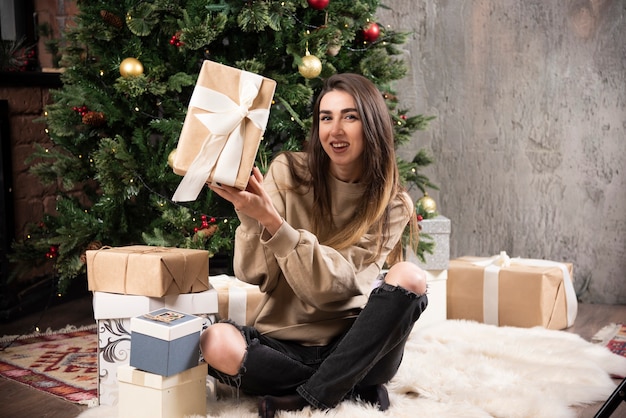 Uśmiechnięta kobieta leżąc na puszystym dywanie z prezentami świątecznymi.