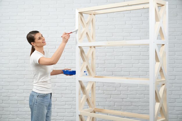 Bezpłatne zdjęcie uśmiechnięta kobieta maluje białe półki drewniane