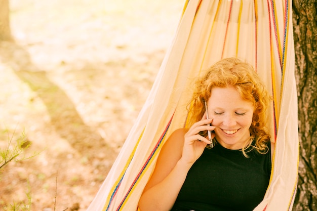 Uśmiechnięta kobieta mówi na telefon w hamaku